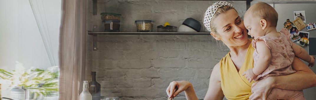 A mom holds and smiles at her baby while she's in the kitchen.